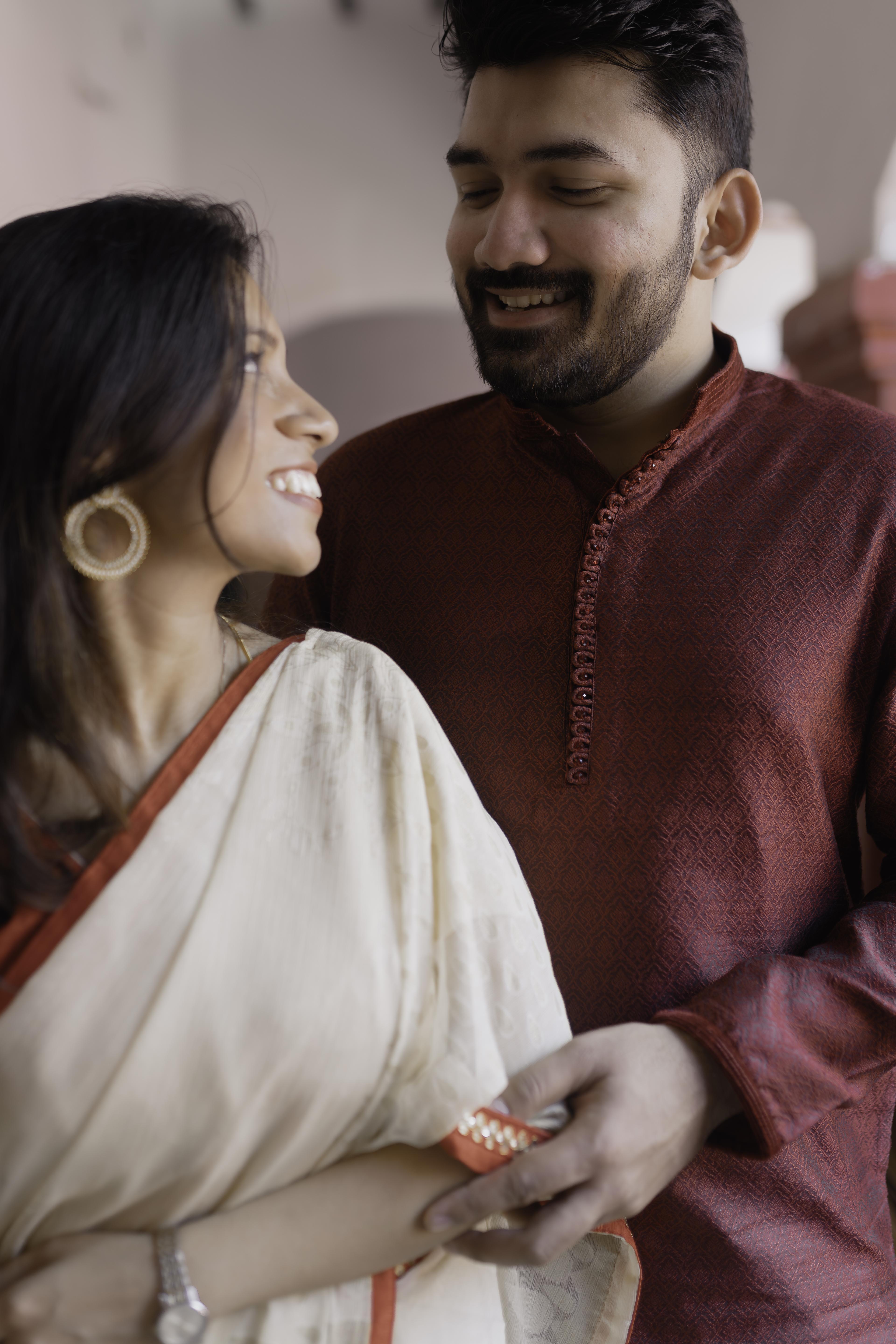 Indian couple sharing intimate moment in natural lighting - bride in white saree and gold hoop earrings smiles at groom wearing maroon kurta - candid pre-wedding photography by CaptureCrewFilms | TCCF