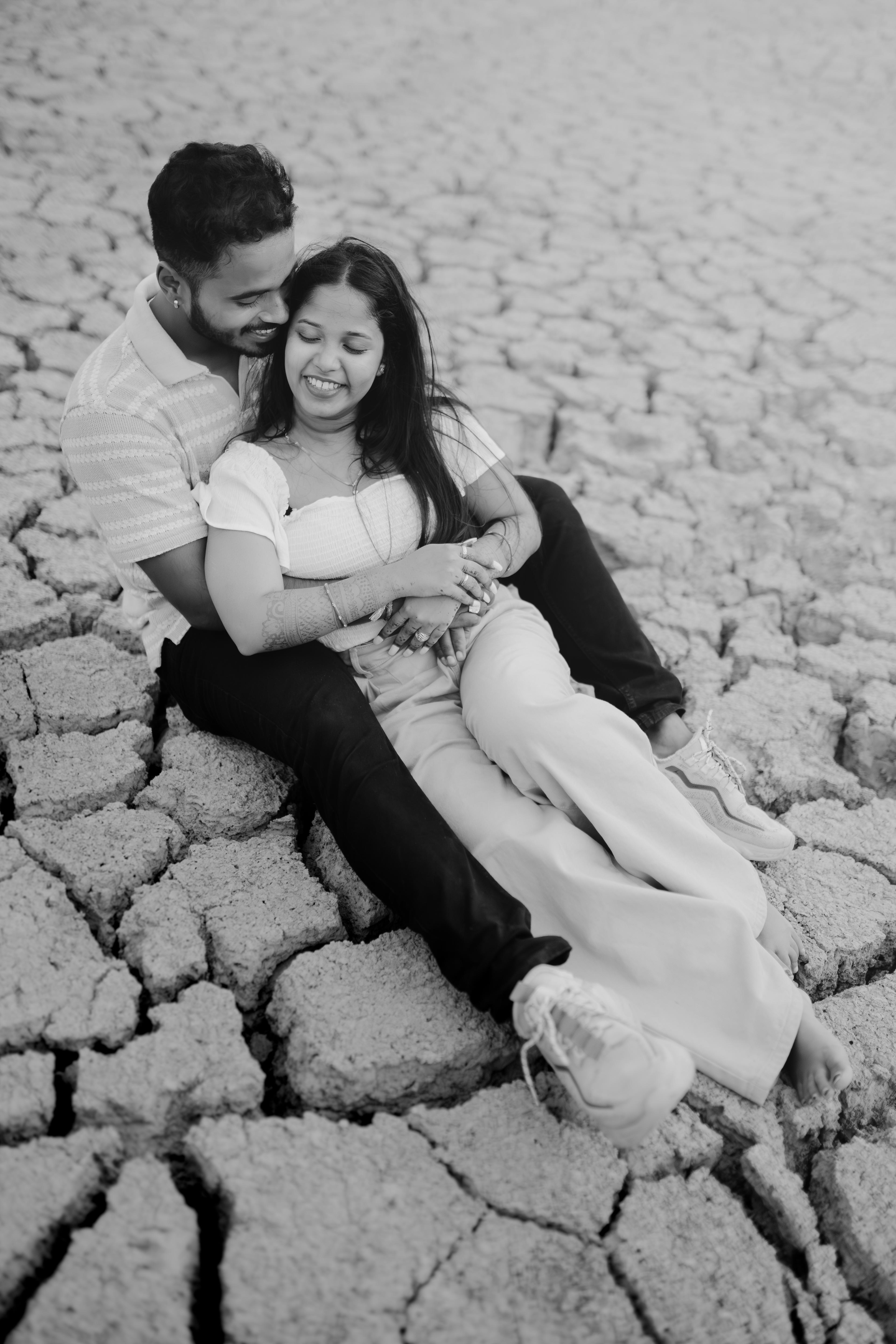 Candid black and white pre-wedding photography - couple embracing on dried lake bed - natural light outdoor couple shoot by CaptureCrew Films | TCCF Photography - romantic engagement session bhubaneswar